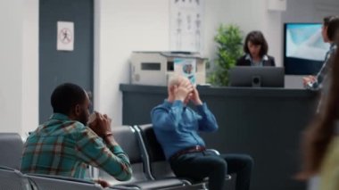 Medical assistant taking african american patient to checkup appointment after sitting in hospital waiting area. Diverse people having medical consultation, waiting in facility lobby. Handheld shot.