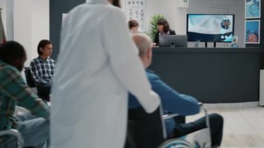 Busy waiting room filled with diverse group of people sitting in row to attend medical examination appointment. Patients in hospital reception lobby waiting area at healthcare clinic.
