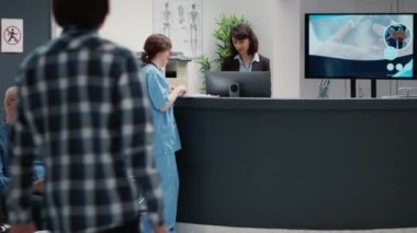 Busy reception desk with many patients waiting to attend consultation, trying to write medical report in hospital lobby. Diverse people having appointments in waiting room area.