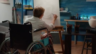 Senior woman with physical impairment drawing vase on canvas to create professional masterpiece design. Wheelchair user dealing with chronic health condition sketching artwork model.