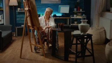 Artist dealing with chronic disability and drawing masterpiece on white canvas, woman with impairment creating artistic masterpiece. Wheelchair user looking at vase to draw sketch.