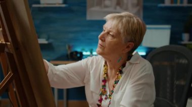 Senior woman using artistic hobby and tools to create artwork design at home, creative skills. Drawing authentic vase model on canvas to do masterpiece on board, art imagination.