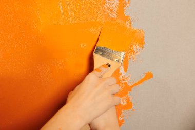 Mother and child holding paintbrush on walls to paint with orange color, renovating apartment room interior with brush and tools. People enjoying painting home space together, paintwork. Close up.