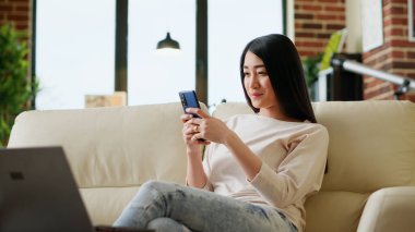 Happy freelancer answering client email on smartphone while working from home. Worker doing remote work while sending messages on mobile phone to coworkers regarding startup project. Handheld shot