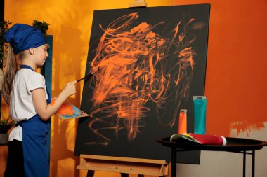 Caucasian child practicing artistic hobby with orange paint and brush to create masterpiece on canvas. Artist with creative vision and skills making artwork design using watercolor aquarelle.