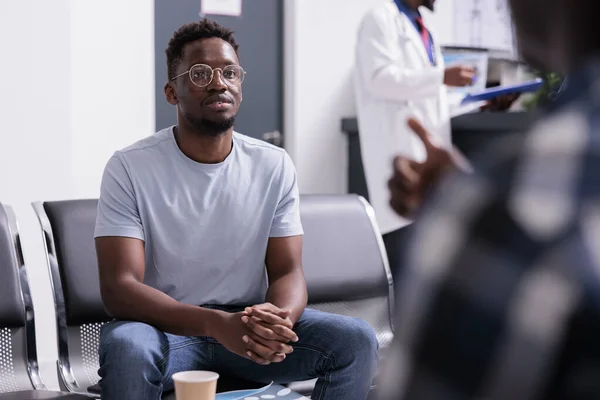 African american patients talking about healthcare and diagnosis in waiting room lobby at health center. Group of men sitting in area at hospital reception before attending checkup examination.