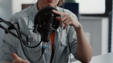 Internet live radio talk show host with headphones talking to audience at microphone in studio. Creative content creator sitting at desk while hosting podcast broadcast in living room.