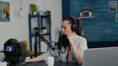 Popular digital content creator sitting at home studio desk while filming vlog. Creative social media influencer hosting show in living room while having modern audio equipment.