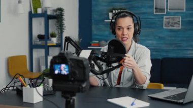 Tech enthusiast presenting VR wearable headset specifications to audience while recording video in living room studio. Vlogger sitting at desk while reviewing futuristic virtual reality goggles.