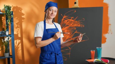Portrait of female artist painting masterpiece on canvas, using watercolor and aquarelle palette with orange color to paint professional artwork. Creating design with artistic skills and vision.