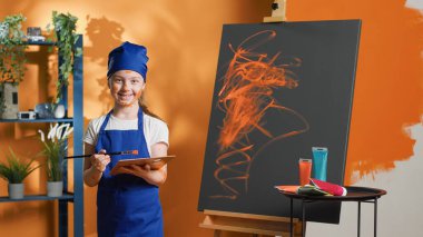 Portrait of little girl using colorful paint to create masterpiece on canvas, painting artwork design with aquarelle palette and paintbrush. Small kid learning to paint with watercolor. Tripod shot.