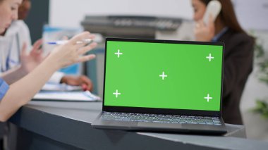 Laptop with greenscreen template at hospital reception desk used by medical staff. Using mockup background with isolated chroma key display and blank copyspace on monitor screen. Close up.