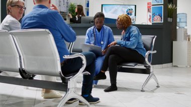 Medical assistant showing disease diagnosis on laptop to young patient sitting in hospital reception waiting area. Female nurse consulting woman at checkup visit appointment, healthcare.