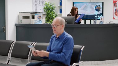 Asian receptionist using reports to help patients with appointments, working at hospital reception counter. Medical worker giving healthcare support to people in waiting room lobby.