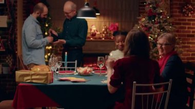 Happy family members gathered in living room to celebrate Christmas together. Cheerful multiethnic people celebrating together winter traditional holiday while talking and feeling good.