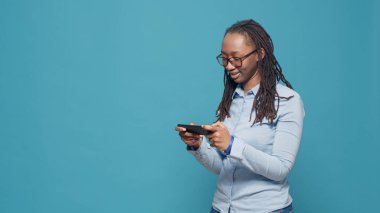 African american gamer playing video games on smartphone, having fun with online gaming competition in front of studio camera. Using mobile phone app to play game on internet website.