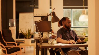 Corporate employee leaving office and waving at colleague, working on business presentation report with data research. Using network information on computer to plan startup project.