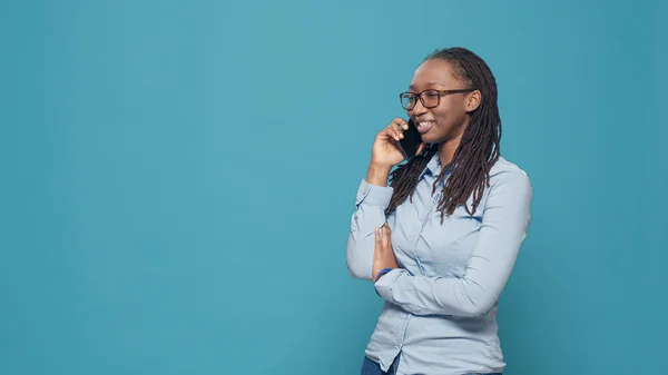 African american woman talking on telephone line, answering phone call over blue background. Person using smartphone to have remote conversation, chatting on mobile phone in studio.