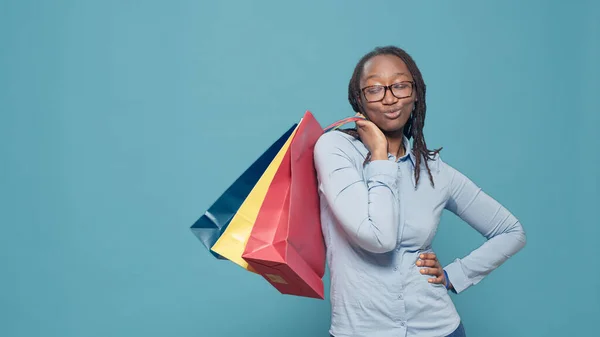 Portrait of female model holding shopping bags after buying clothes on sale discount from retail store at mall. Shopaholic woman paying to buy things in colorful paperbags, posing.