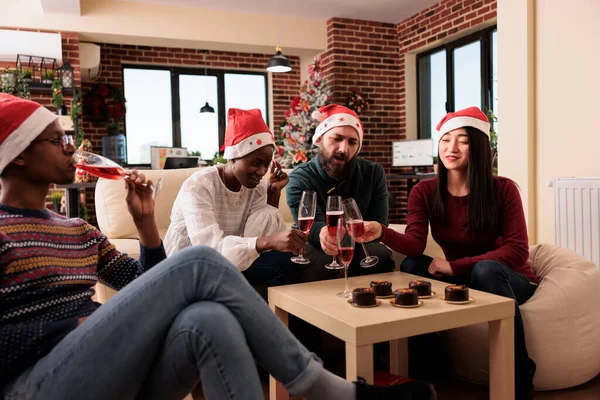 Coworkers clinking glasses of wine at xmas office event, giving toast with alcohol to celebrate christmas eve festivity with decorations. Doing cheers gesture with alcoholic drinks, holiday party.