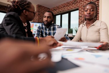African american employees doing teamwork at job, working with startup documents to plan business presentation and report with research data. Analyzing paperwork documents in boardroom.