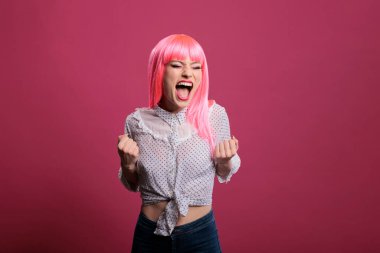 Lucky confident lady celebrating big win and success, posing in front of camera over pink background. Feeling happy and excited about achievement and wonderful triumph, winner style.