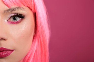 Attractive beauty model showing half of face on camera in studio, having pink hair and makeup cosmetics. Stylish cute woman feeling sensual and carefree, having fun over background. Close up.