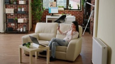 Beautiful smiling woman taking selfie photos with modern smartphone while sitting at home on sofa. Attractive young adult person with modern mobile phone taking pictures of herself.