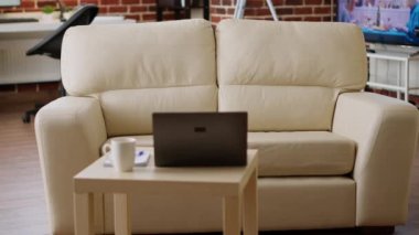 Empty brick wall house with nobody in it and with modern portable computer on desk. Interior of modern and cozy apartment living room with comfortable sofa and laptop on coffee table