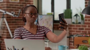 Young woman taking photos on smartphone app during break, working from home on startup business. Female freelancer taking pictures and capturing photography, remote laptop work.