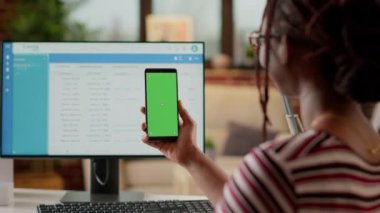 Company employee looking at smartphone display with greenscreen, doing remote job at home. Using isolated chroma key copyspace with blank mockup template and mobile phone background.