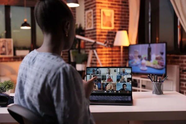 Remote team brainstorming, having conversation on online business meeting. African american female corporate worker chatting with colleagues on videocall and looking on laptop screen