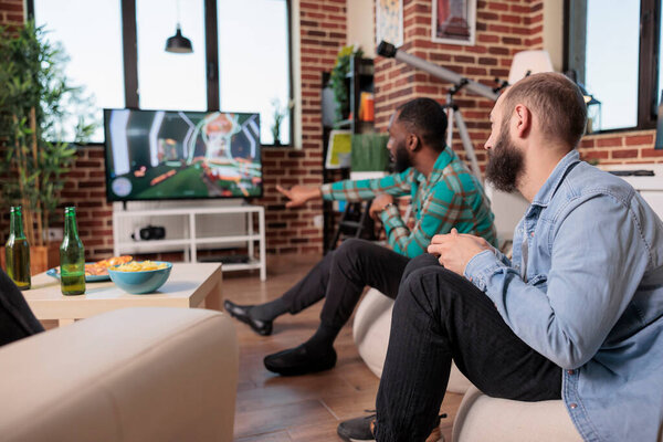 Diverse team of men using tv console to play shooter video games, having fun with gaming competition on television. People enjoying teamwork strategy, relaxing with leisure activity.