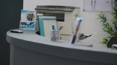 Hospital reception counter with computer and printer to help with medical appointments and healthcare insurance support. Empty registration desk in lobby to fill in checkup reports and forms.