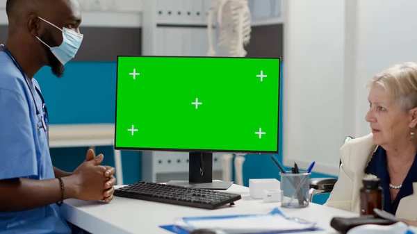 Male nurse and patient wheelchair user looking at greenscreen on monitor, isolated display. Man and senior paralyzed woman using chromakey mockup template with blank copyspace background.
