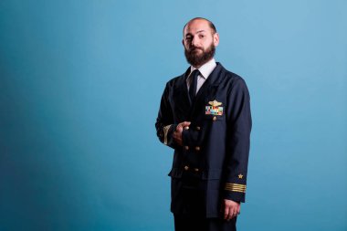 Uçak pilotu üniformalı bir portre giyiyor, kendine güvenen bir kaptan ayakta duruyor, kameraya bakıyor, orta ölçekli stüdyo görüntüsü. Profesyonel takım elbiseli, ciddi yakışıklı bir havacı.