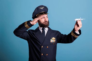 Küçük uçak modelini selamlayan üniformalı pilot, yolcu uçağıyla oynayan uçak kaptanı. Ceketinde kanat rozeti olan ciddi bir uçak mürettebatı üyesi.