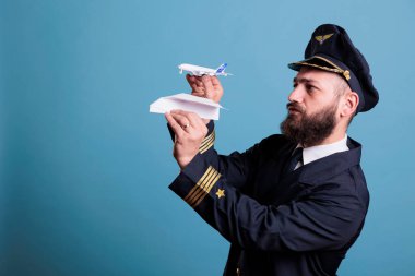 Jet oyuncağı ve kağıt uçağı elinde tutan uçak pilotu uçak modeliyle uçak kazasını gösteriyor. Mavi arka planda profesyonel havacılık akademisi havacısı