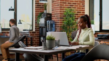 Afrika kökenli Amerikalı bir kadın, ödevleri ve laptopları analiz ediyor. İş projesi üzerinde çalışıyor. Veri araştırması yapıyor. Çevrimiçi ağ sunumu kullanan kadın çalışan.