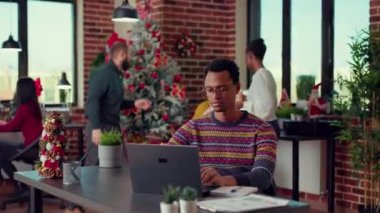 Ofisteki bayram şenliği sırasında dizüstü bilgisayardaki araştırma verilerini analiz eden çalışanın portresi. Bilgisayar üzerinde çalışmak ve Noel arifesini mevsimlik süslerle ve dekorlarla kutlamak..