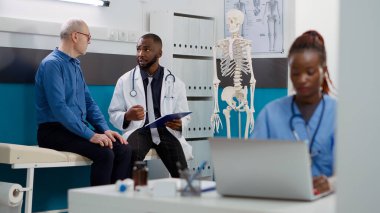 Genel pratisyen hekim doktor muayenesinde yaşlı bir adama hastalık konusunda danışmanlık yapıyor. Sağlık uzmanı hastaya danışmanlık yapıyor, profesyonel tavsiyelerde bulunuyor..