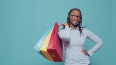 Portrait of female model holding shopping bags after buying clothes on sale discount from retail store at mall. Shopaholic woman paying to buy things in colorful paperbags, posing.