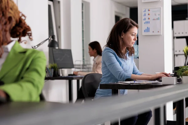 忙碌的公司员工在办公桌前共同工作 公司经理在工作场所 侧视图 在现代办公室的笔记本电脑上有吸引人的严肃女性打字 有选择的焦点 — 图库照片