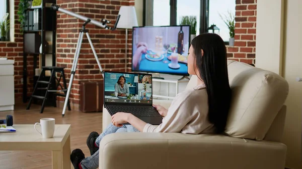 Young adult person with portable computer doing remote work while talking on online meeting. Woman sitting on couch working remotely while discussing with office manager on videocall conference