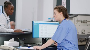 Resepsiyondaki hasta randevuları üzerinde çalışan tıbbi asistan, Afrikalı Amerikalı doktorlara kıdemli bir adamla istişarede bulunmaları için yardım ediyor. Sağlık hizmetleri kliniğinde çeşitli personel.