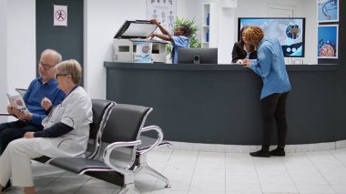 Young patient having appointment with medic at medical facility, filling in report papers to attend checkup visit examination. Receptionist helping woman sitting in waiting room.