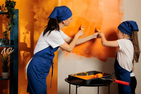 オレンジ色のペイントと絵筆で大人と子供の絵画は 家の改装作業を一緒に楽しみのために動作します 家を改装し 金型や機器を飾る使用して幸せな人々 — ストック写真