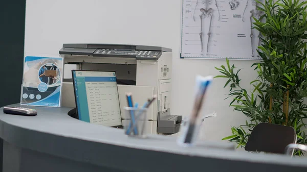 Hospital reception counter with computer and printer to help with medical appointments and healthcare insurance support. Empty registration desk in lobby to fill in checkup reports and forms.