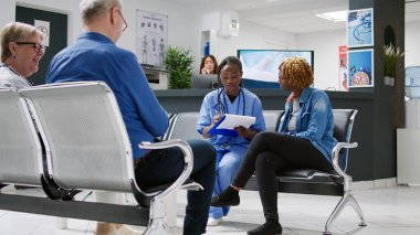 African american nurse doing consultation with patient in waiting area lobby, taking notes on checkup papers to give treatment and medicine. Medical assistant and woman talking about healthcare.