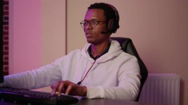 Oyun kulaklığı takmış Afrika kökenli Amerikalı oyuncunun profesyonel bilgisayar oyununda çok oyunculu takım üyeleriyle konuşması. Çevrimiçi yarışma sırasında bilgisayar ekranına bakan adam.